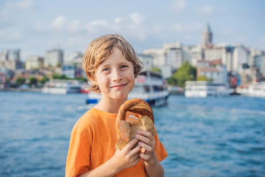 Boy in Istanbul having breakfast with Simit and a glass of Turkish tea. Glass of Turkish tea and bagel Simit against golden horn bay and the Galata Tower in Istanbul, Turkey. Turkiye. Traveling with kids concept.