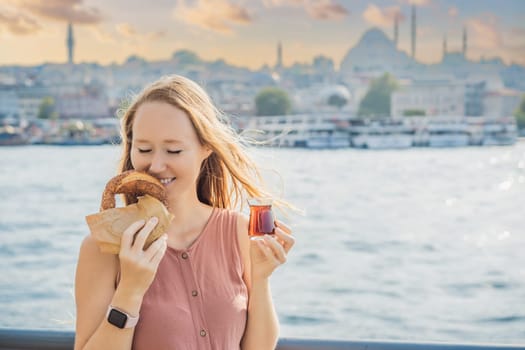 Woman in Istanbul having breakfast with Simit and a glass of Turkish tea. Glass of Turkish tea and bagel Simit against golden horn bay in Istanbul, Turkey. Turkiye.
