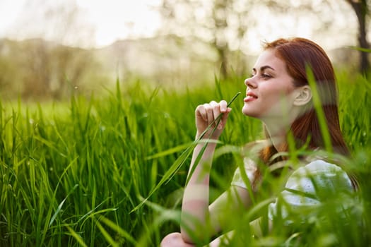 portrait of a blissfully smiling woman sitting in the grass with a leaf in her hand. High quality photo