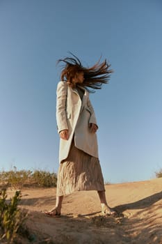 stylish woman in fashion style posing on the sand covering her face with her hair in motion. High quality photo