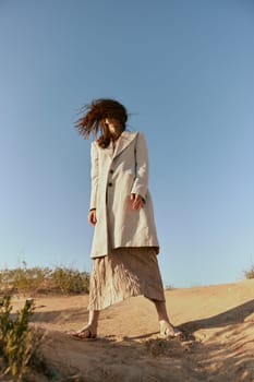 stylish woman in fashion style posing on the sand covering her face with her hair in motion. High quality photo