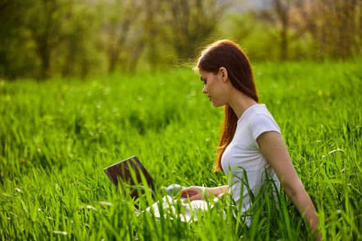 a woman with laptop sitting in a city park on the lawn on a hot summer day. High quality photo