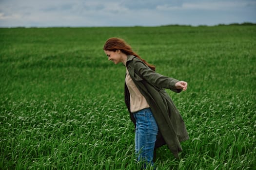 red-haired, happy woman stands in a green field in rainy weather. Emotions, harmony with nature. High quality photo