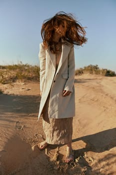 a woman with long red hair blown in the wind stands in stylish clothes on the sand. High quality photo