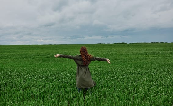 a woman in a long coat stands in a green field on a cloudy day with her hands up to the sky. High quality photo
