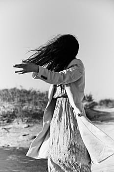 monochrome photo of a twirling woman on the coast in a light-colored jacket