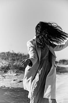 monochrome photo of a twirling woman on the coast in a light-colored jacket