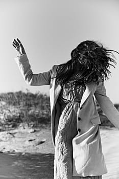 monochrome photo of a twirling woman on the coast in a light-colored jacket