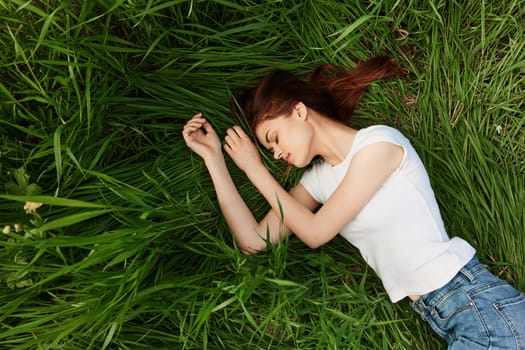 a red-haired woman lies in the tall grass in a white T-shirt and jeans. High quality photo