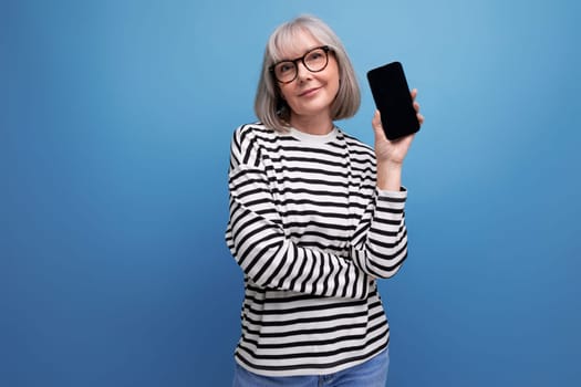middle-aged youth 60s woman holding a smartphone with a mockup on a bright background with copy space.