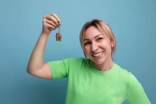 horizontal photo of a young mother in a casual outfit who holds a keychain from the keys of the apartment on a blue background.