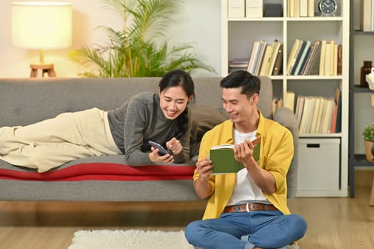 Image of happy married young couple reading book, enjoying leisure time on weekend at home.