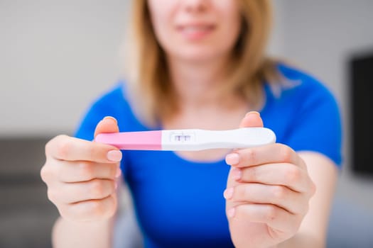 Blonde smiling woman holding a positive pregnancy test.