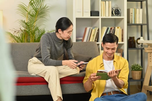 Happy young couple enjoying carefree leisure weekend time, reading book in cozy living room.