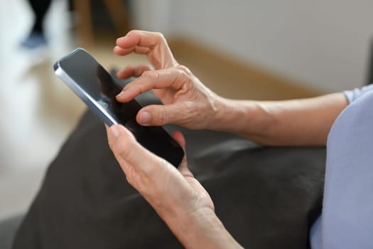 Close up view of senior woman hand holding smart phone, browsing wireless internet or chatting online.