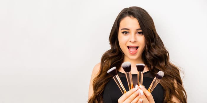 Gorgeous young woman holding a set of cosmetic brushes for professional makeup on a white background with copy space.