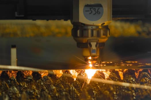 Contemporary laser cutter carves thin metal sheet with bright sparks in dark workshop of modern production plant extreme closeup