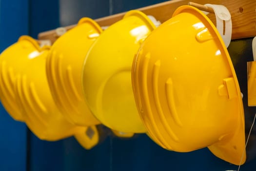 Line of new yellow protective helmets for workers hangs on wooden bar in dressing room of production plant extreme close view