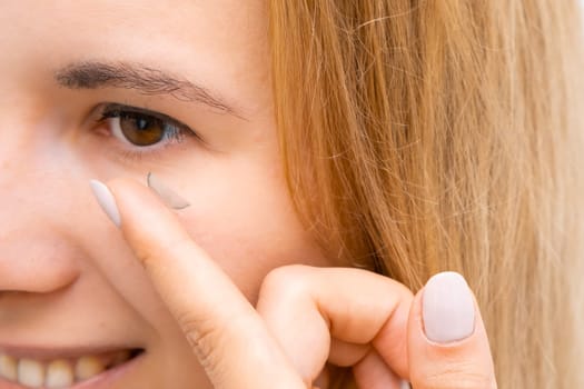 Side view of a smiling woman applying contact eye lenses.