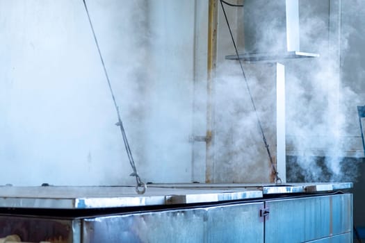Large oven closed with metal lids and rising up hot steam cloud in spacious workshop of old traditional glassblowing plant