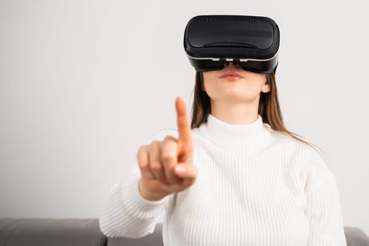 Brunette girl touching air with a finger in VR glasses. Metaverse technology concept.