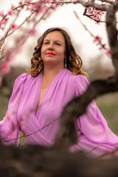 Woman peach blossom. Happy curly woman in pink dress walking in the garden of blossoming peach trees in spring.