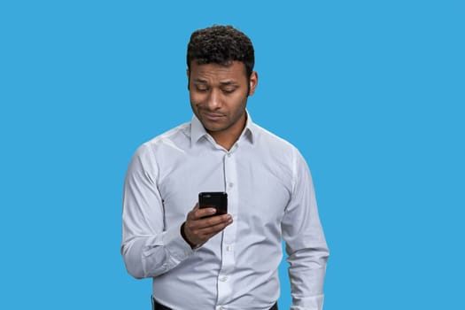 Portrait of brown indian man typing message on his smartphone. Isolated on blue.