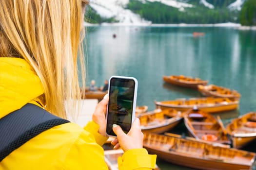 Travel blogger and tourist taking photo of boats on Lake Braies in the Dolomites Alps.