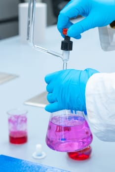 Close up laboratory worker uses a titration method of analysis to study chemical properties of the water sample. Scientist holding Erlenmeyer flask with pink solution