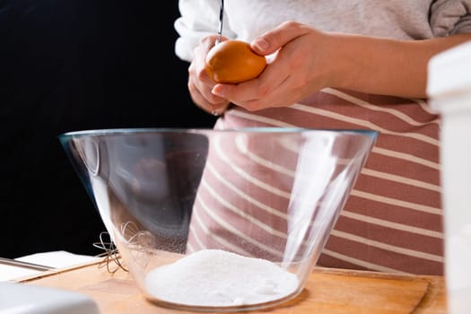 The dough preparation process. Female hands break an egg into flour in a bowl for baking on a black background.