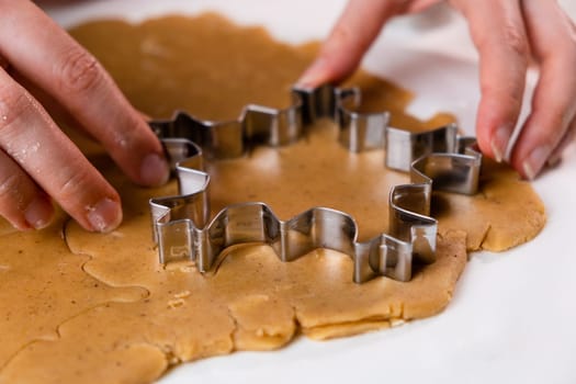 Close up woman hands cutting out cookies with metal mold from the shortcrust pastry. A metal forms in the form of snowflakes for making gingerbread for Christmas.