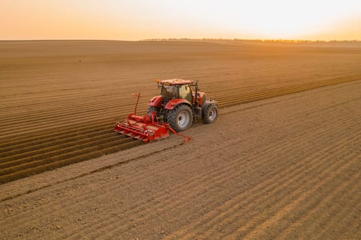 PRAGUE , CZECH REPUBLIC - MARCH 18 2022: Agricultural machine prepares long beds for planting potatoes on cultivated field. Red tractor works dragging plow behind aerial view