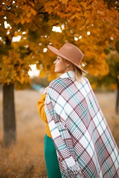 autumn woman in a green dress, brown hat, plaid, against the background of an autumn tree.