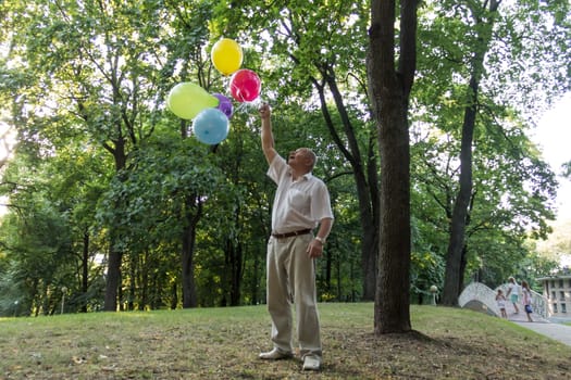 An old man is playing in the park with bright, balloons on his birthday.