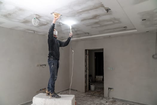 sanding a plasterboard ceiling in a new building with a trowel. High quality photo