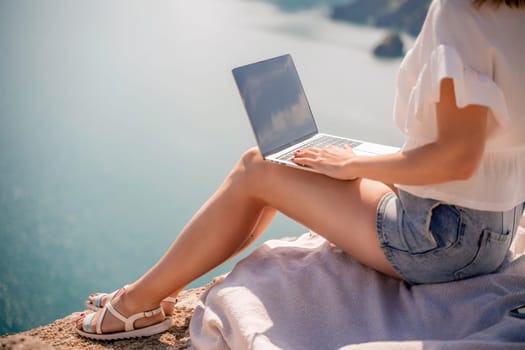 Freelance women sea working on the computer. Good looking middle aged woman typing on a laptop keyboard outdoors with a beautiful sea view. The concept of remote work