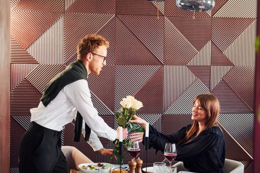 Waiter gives flowers to a woman. Indoors of new modern luxury restaurant.