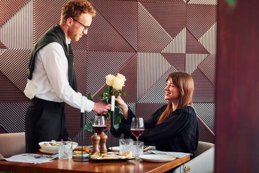 Waiter gives flowers to a woman. Indoors of new modern luxury restaurant.