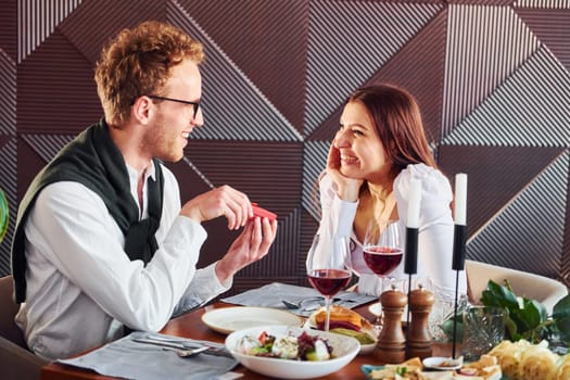 Young guy makes proposal to a woman. Indoors of new modern luxury restaurant.