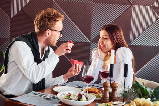 Young guy makes proposal to a woman. Indoors of new modern luxury restaurant.