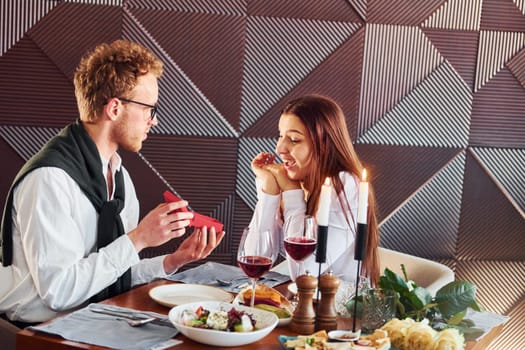 Young guy makes proposal to a woman. Indoors of new modern luxury restaurant.