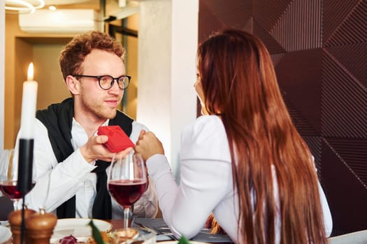 Young guy makes proposal to a woman. Indoors of new modern luxury restaurant.