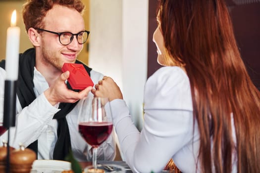 Young guy makes proposal to a woman. Indoors of new modern luxury restaurant.