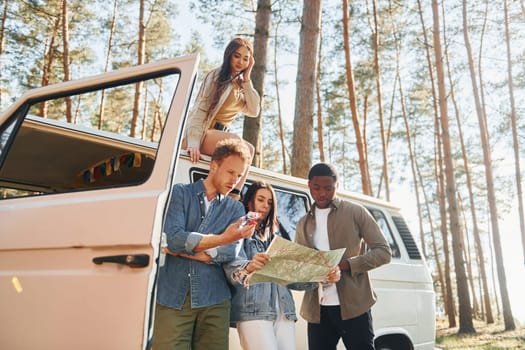 Using map. Group of young people is traveling together in the forest at daytime.