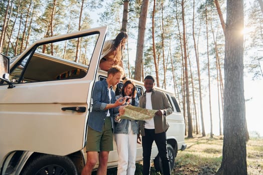 Using map. Group of young people is traveling together in the forest at daytime.