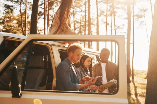 Using map. Group of young people is traveling together in the forest at daytime.