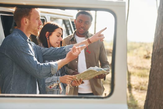 Holding map and looking for location. Group of young people is traveling together in the forest.