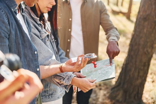 Holding map and looking for location. Group of young people is traveling together in the forest.