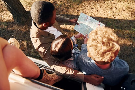 Holding map and looking for location. Group of young people is traveling together in the forest.