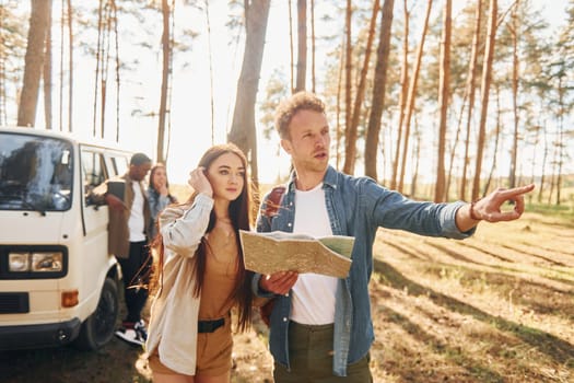 Standing near the car. Group of young people is traveling together in the forest at daytime.